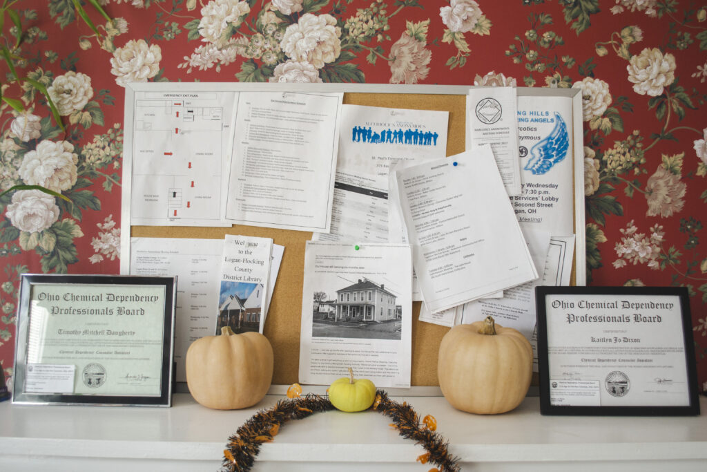 Photo of bulletin board with recovery meeting flyers. small pumpkins sit on the mantle the bulletin board is resting on