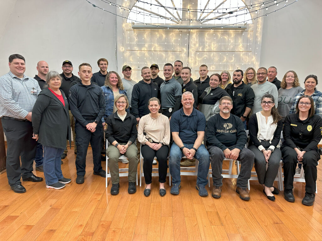 The 2023 CIT graduating class poses in front of twinkle lights alongside the CIT coordinators in the meeting room of the Dairy Barn Arts Center.